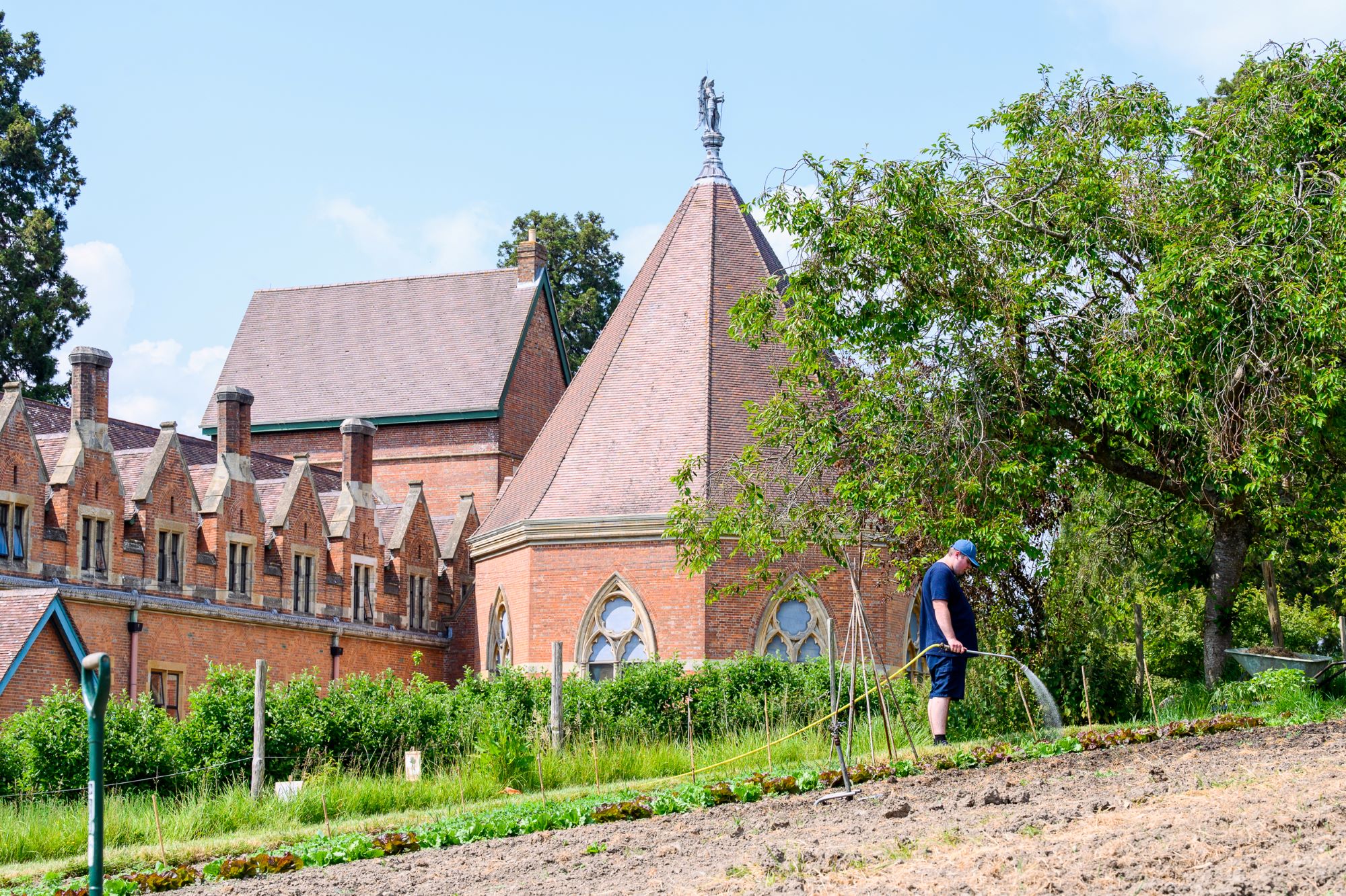 A student watering the garden with The Mount House in the background