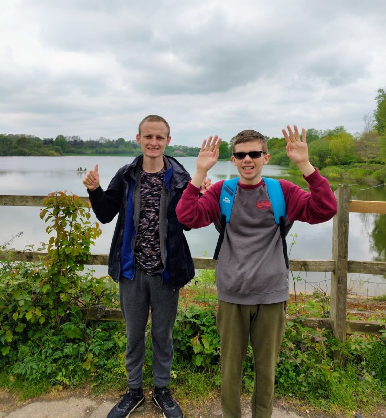 Two students standing in front of a lake with thumbs up